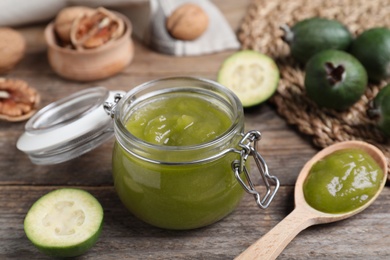 Photo of Glass jar of tasty feijoa jam on wooden table, closeup