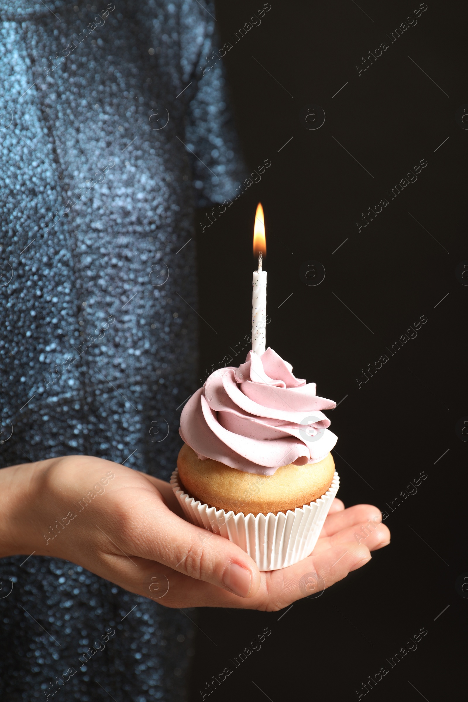 Photo of Woman holding delicious birthday cupcake with burning candle on black background, closeup