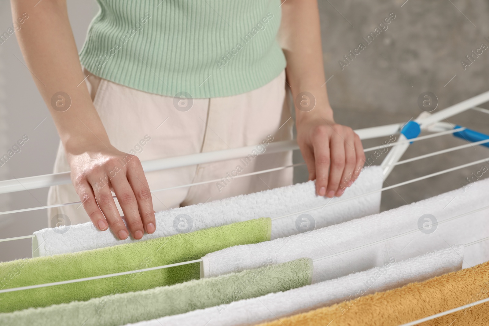 Photo of Woman hanging clean terry towels on drying rack indoors, closeup