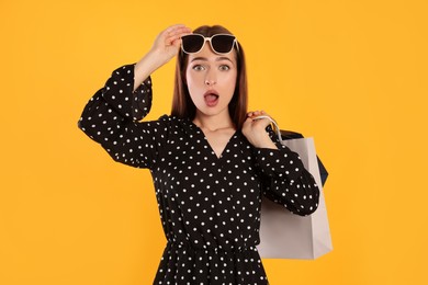 Photo of Surprised young woman with shopping bags on yellow background. Big sale