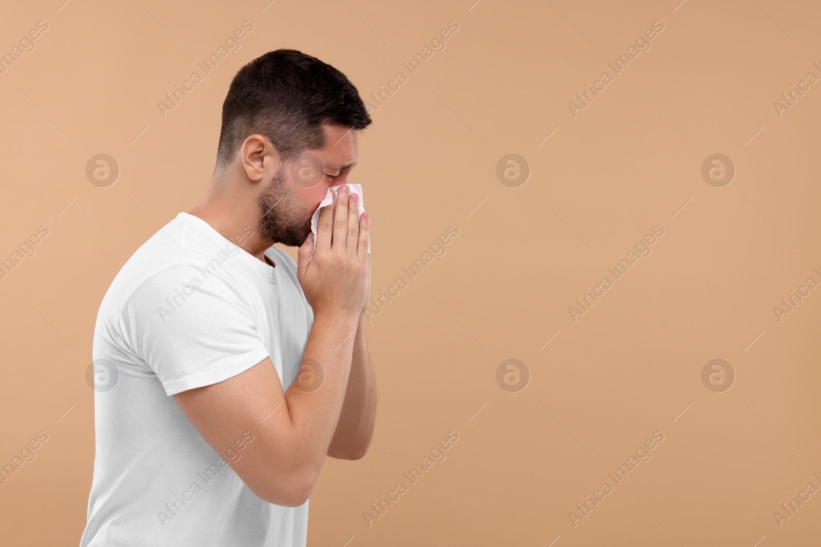 Photo of Allergy symptom. Man sneezing on light brown background. Space for text