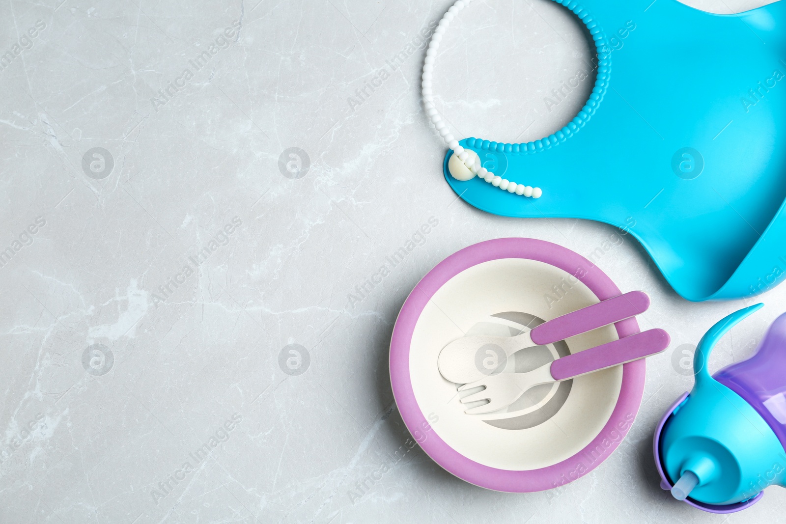 Photo of Set of colorful plastic dishware and silicone bib on light grey marble table, flat lay with space for text. Serving baby food