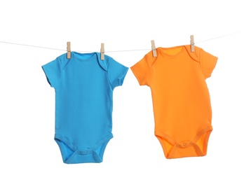 Photo of Colorful baby onesies hanging on clothes line against white background. Laundry day