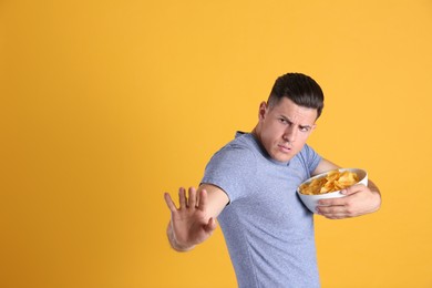 Photo of Greedy man hiding bowl with chips on yellow background, space for text