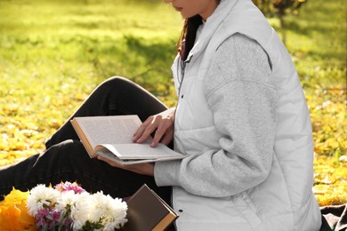 Photo of Woman reading book outdoors in park on autumn day, closeup
