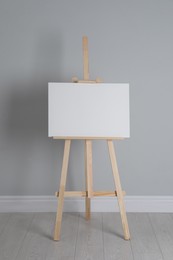 Wooden easel with blank canvas near light wall