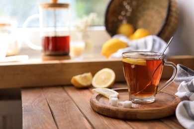 Photo of Glass cup with delicious tea, sugar and lemon on wooden table, space for text