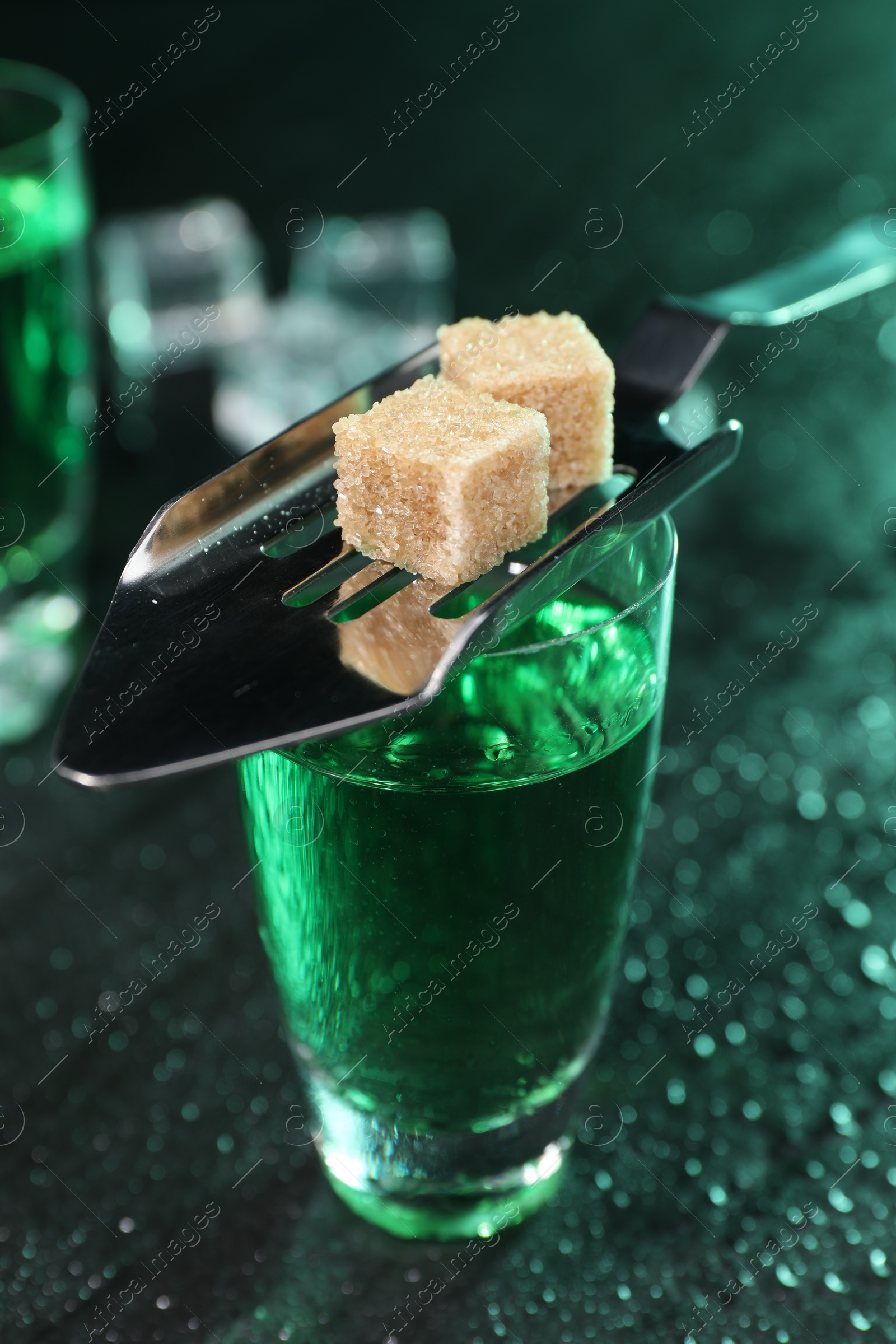 Photo of Absinthe in shot glass, spoon and brown sugar cubes on gray table, closeup. Alcoholic drink