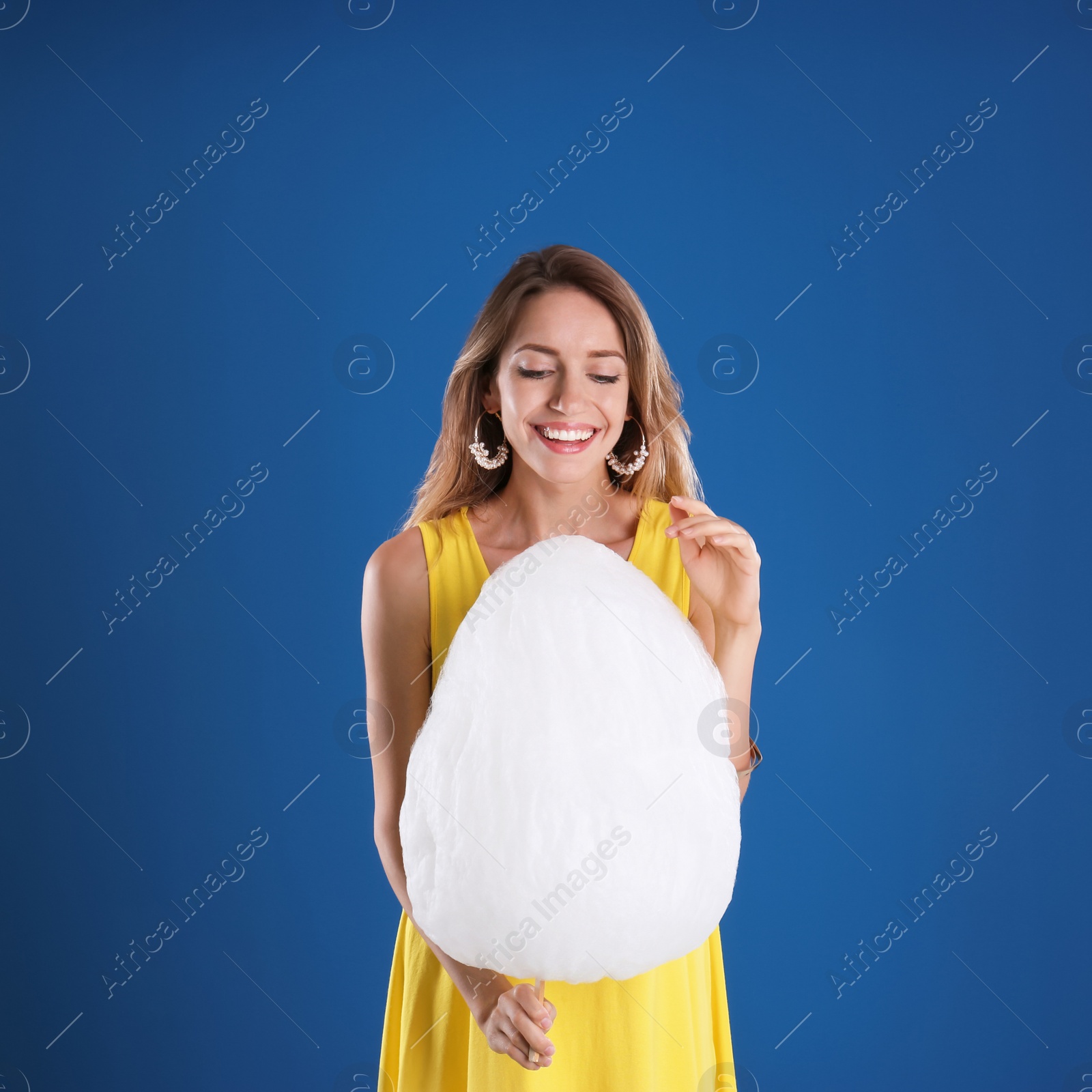 Photo of Happy young woman with cotton candy on blue background