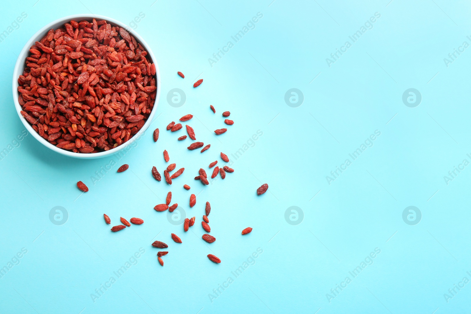 Photo of Bowl of dried goji berries on light blue background, top view with space for text. Healthy superfood