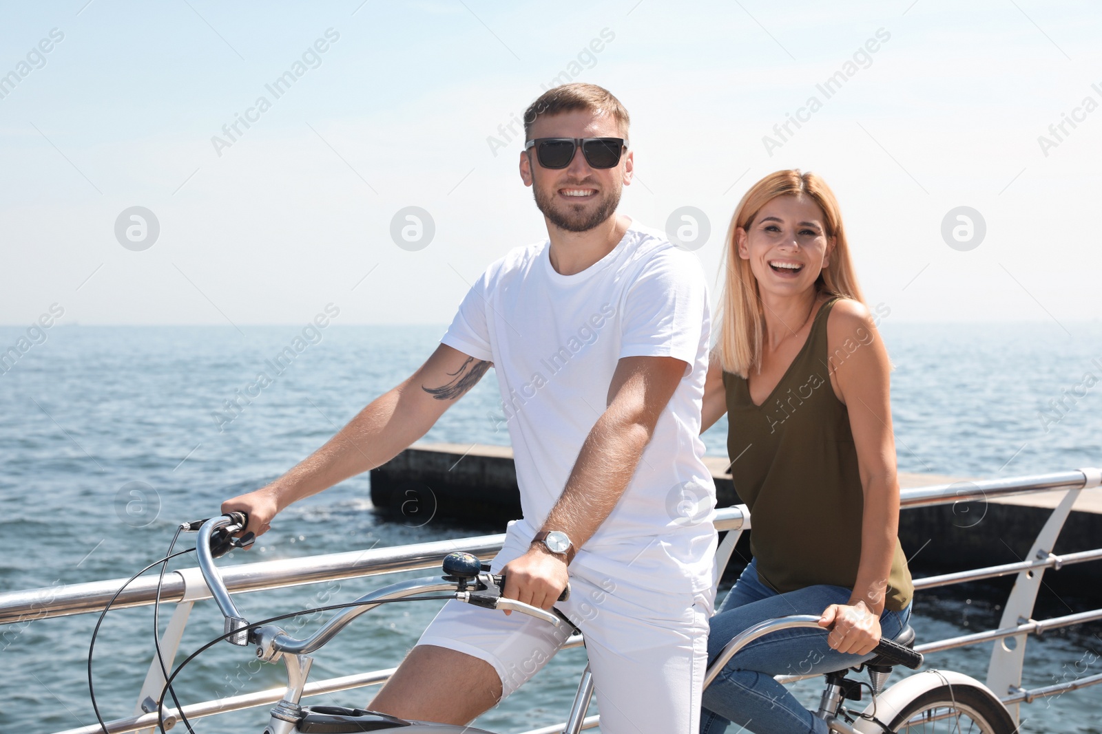 Photo of Couple riding tandem bike near sea on sunny day