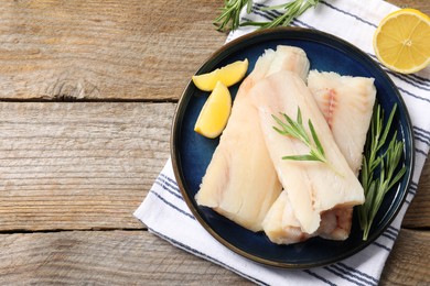 Photo of Pieces of raw cod fish, rosemary and lemon on wooden table, top view. Space for text
