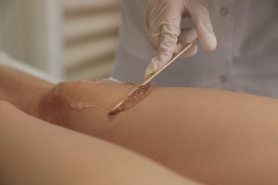 Photo of Professional cosmetologist applying gel on client's leg before laser epilation procedure in salon, closeup