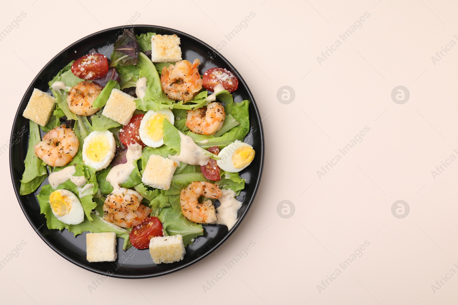 Photo of Delicious Caesar salad with shrimps on beige table, top view. Space for text
