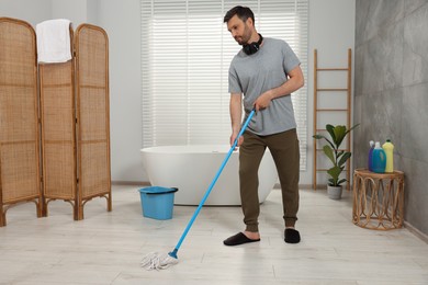 Photo of Handsome man cleaning floor with mop in bathroom