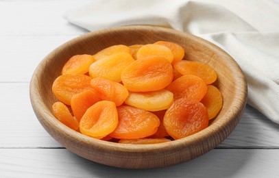 Photo of Bowl of tasty apricots on white wooden table. Dried fruits