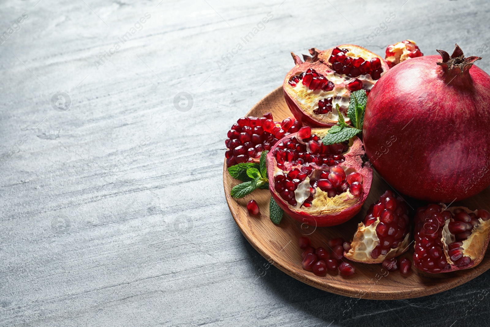 Photo of Plate with ripe pomegranates on grey background. Space for text