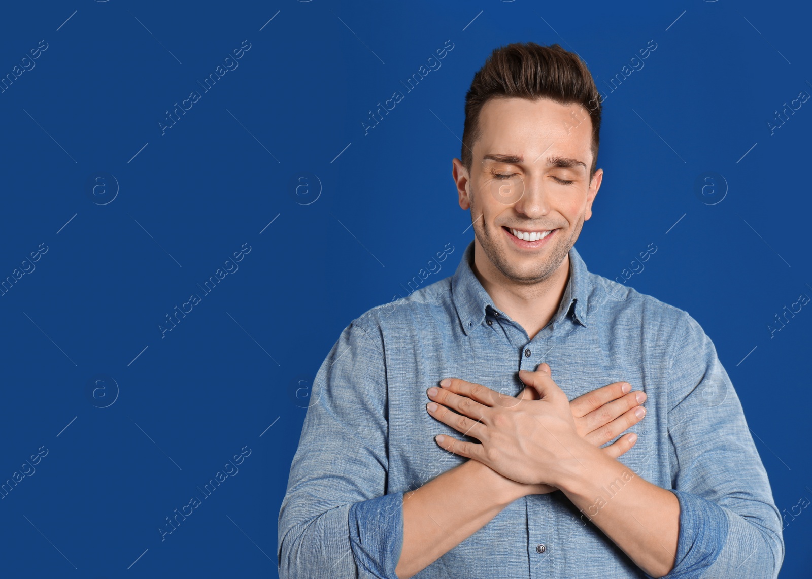 Photo of Handsome grateful man with hands on chest against blue background