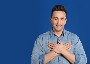 Handsome grateful man with hands on chest against blue background