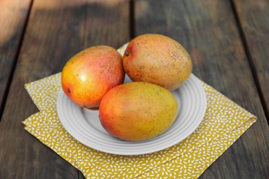 Plate with tasty mangoes on wooden table outdoors