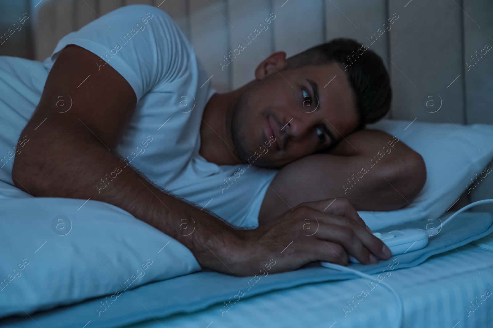 Photo of Man switching on electric heating pad in bed at night