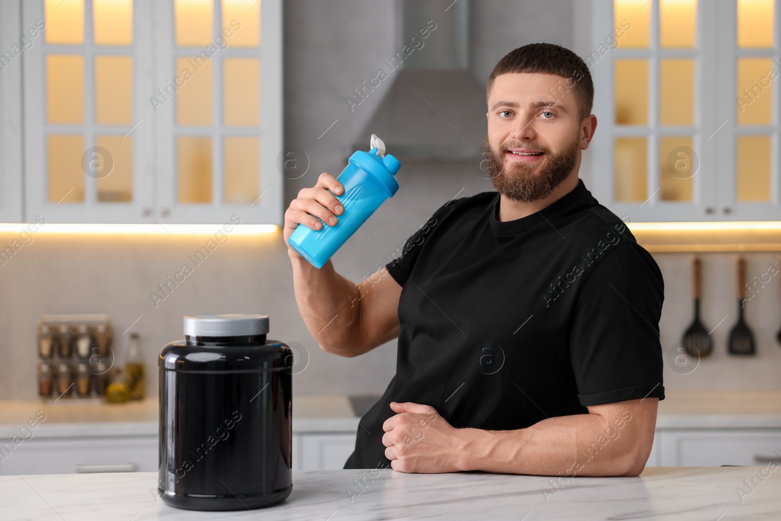 Photo of Young man with shaker of protein and powder at white marble table in kitchen