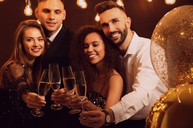 Photo of Happy friends celebrating New Year indoors, focus on hands with glasses of sparkling wine 