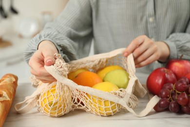 Photo of Woman with string bag of fresh fruits at light marble table, closeup