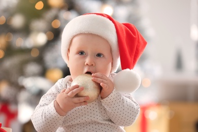 Little baby in Santa hat playing with Christmas balls indoors