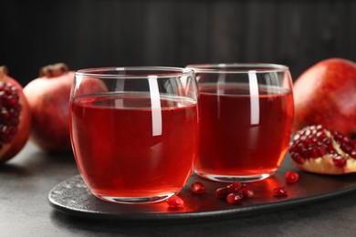 Photo of Tasty pomegranate juice in glasses and fresh fruits on grey table, closeup