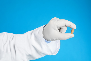 Doctor holding suppository for hemorrhoid treatment on blue background, closeup