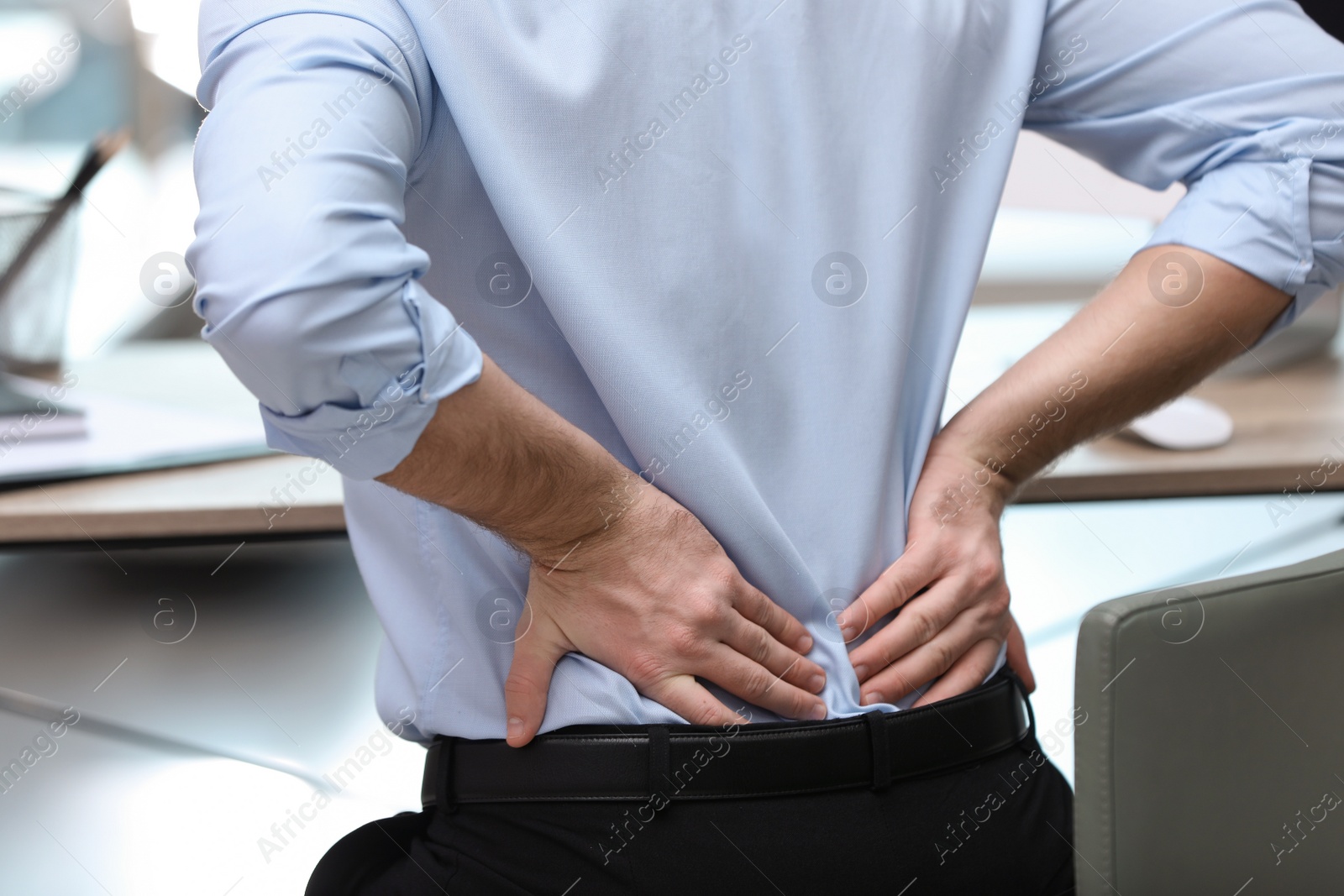 Photo of Businessman suffering from back pain at workplace, closeup