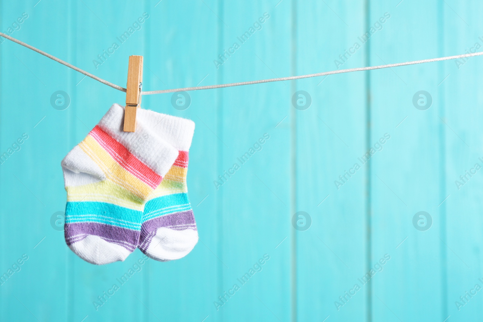 Photo of Baby socks on laundry line against color wooden background, space for text. Child accessories