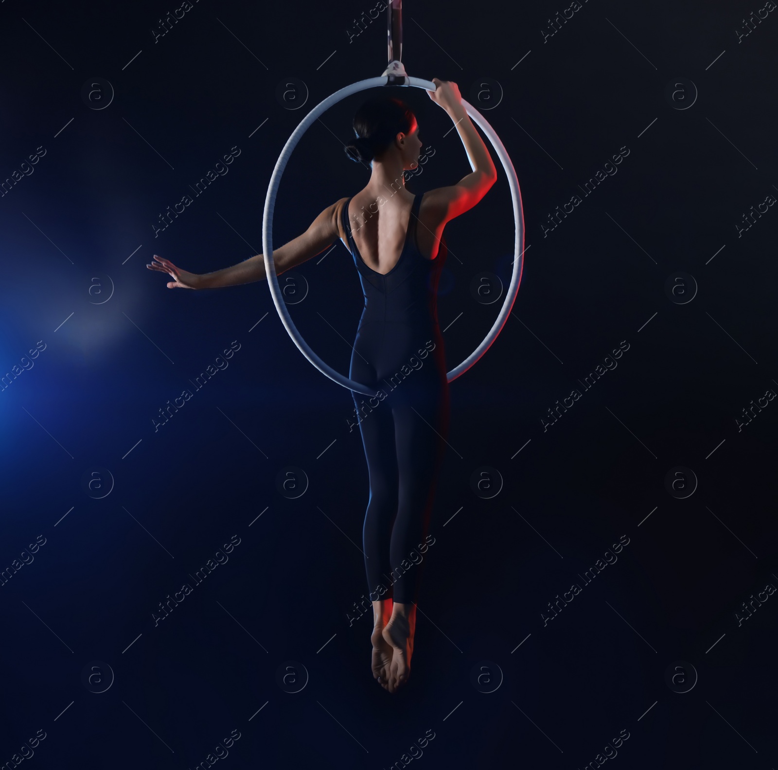 Photo of Young woman performing acrobatic element on aerial ring against dark background