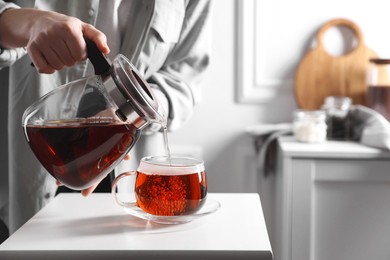 Woman pouring hot tea into cup at white table, closeup