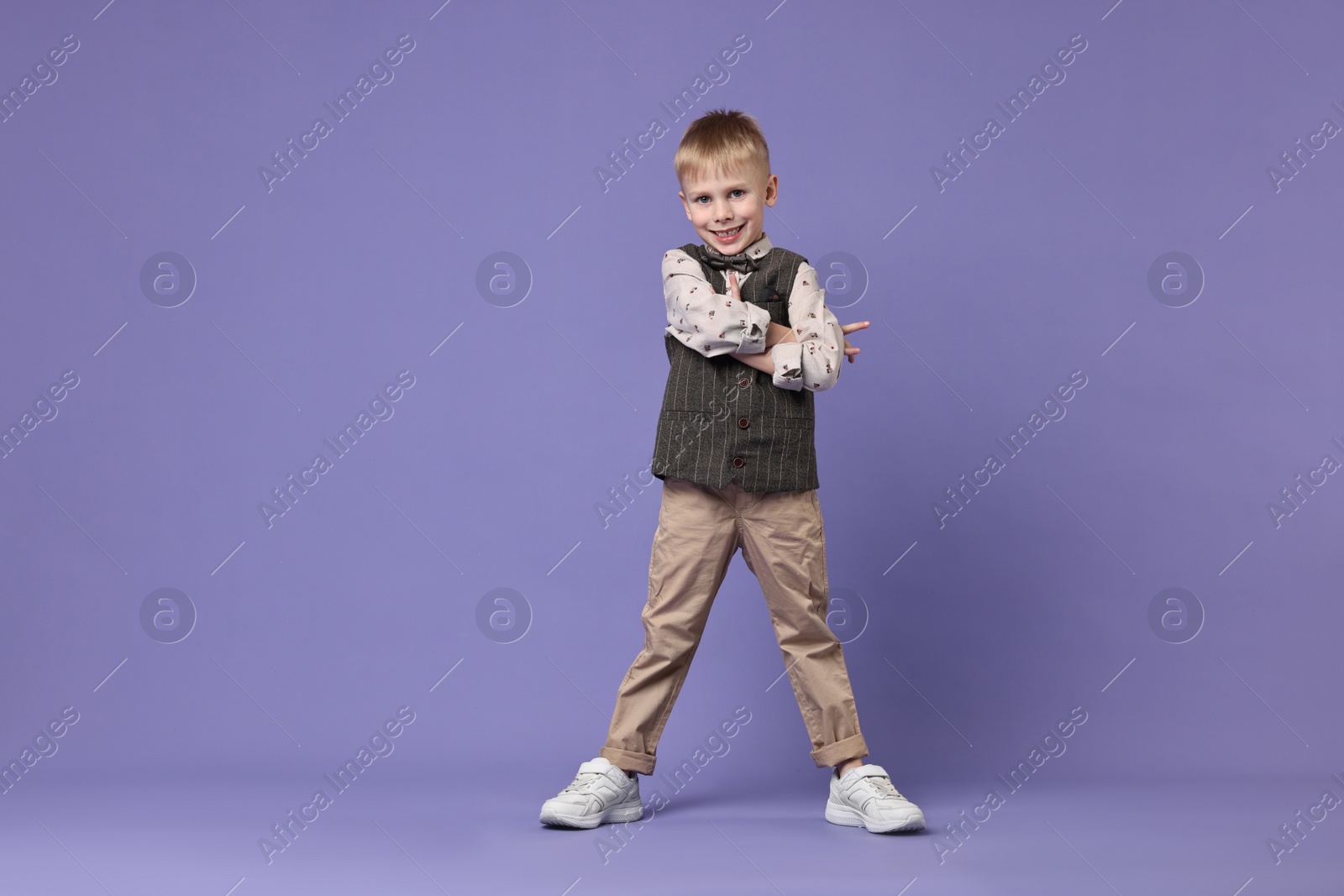 Photo of Happy little boy dancing on violet background. Space for text