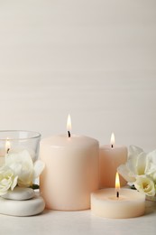 Beautiful composition with burning candles, spa stones and flowers on white table. Space for text