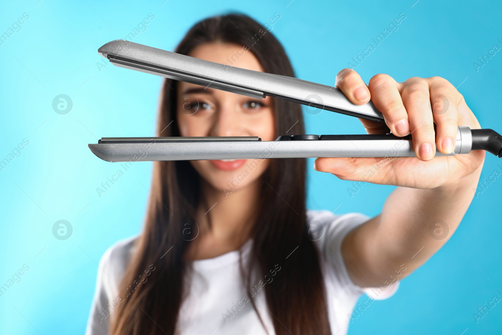 Photo of Happy woman with hair iron on color background