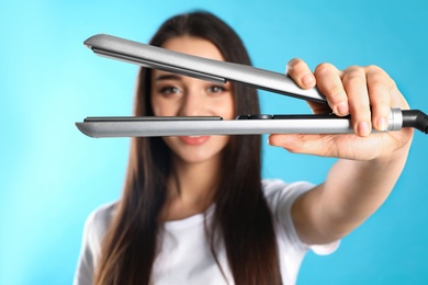 Happy woman with hair iron on color background