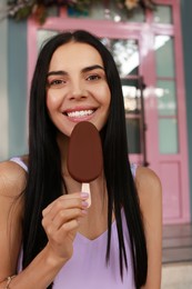 Photo of Beautiful young woman holding ice cream glazed in chocolate on city street