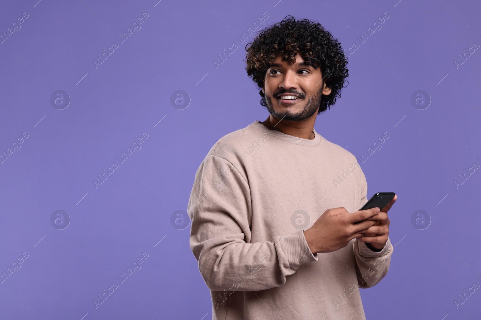 Photo of Handsome smiling man using smartphone on violet background, space for text