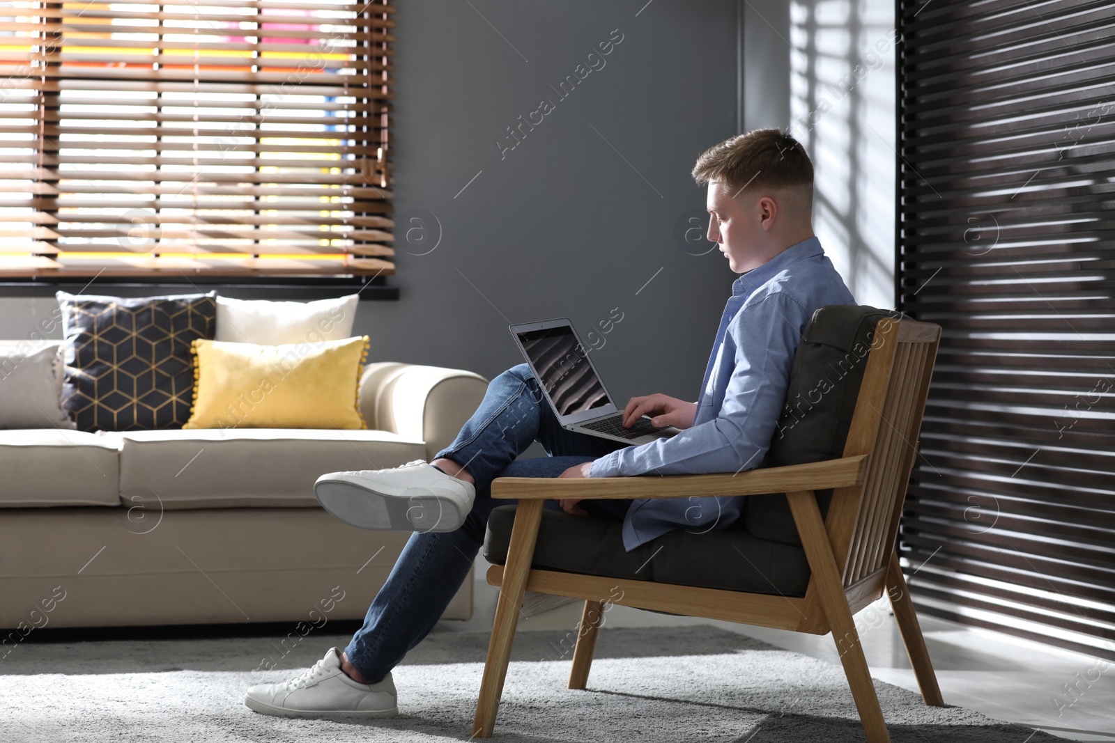 Photo of Teenage boy with laptop sitting in armchair at home