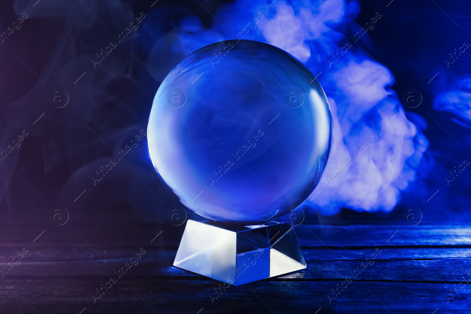 Photo of Magic crystal ball on wooden table and smoke against dark background. Making predictions