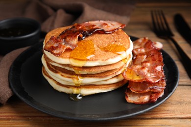 Photo of Delicious pancakes with maple syrup and fried bacon on wooden table, closeup