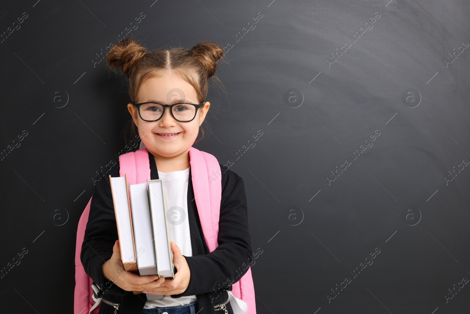 Photo of Happy little school child with books near chalkboard. Space for text