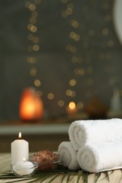 Spa composition. Rolled towels, sea salt and burning candles on table against blurred lights, space for text