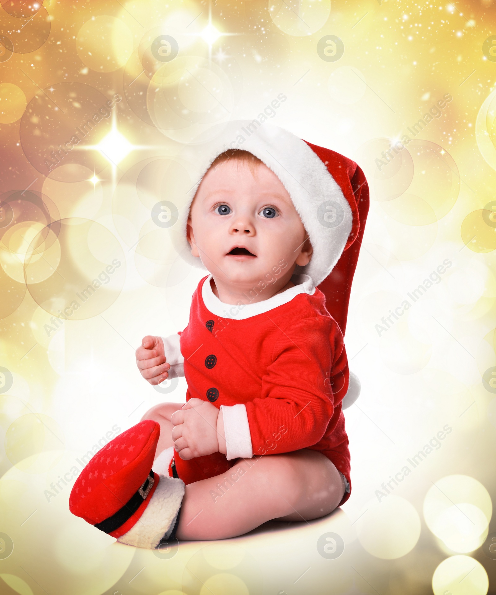 Image of Cute little baby in Santa Claus costume against blurred festive lights. Christmas celebration