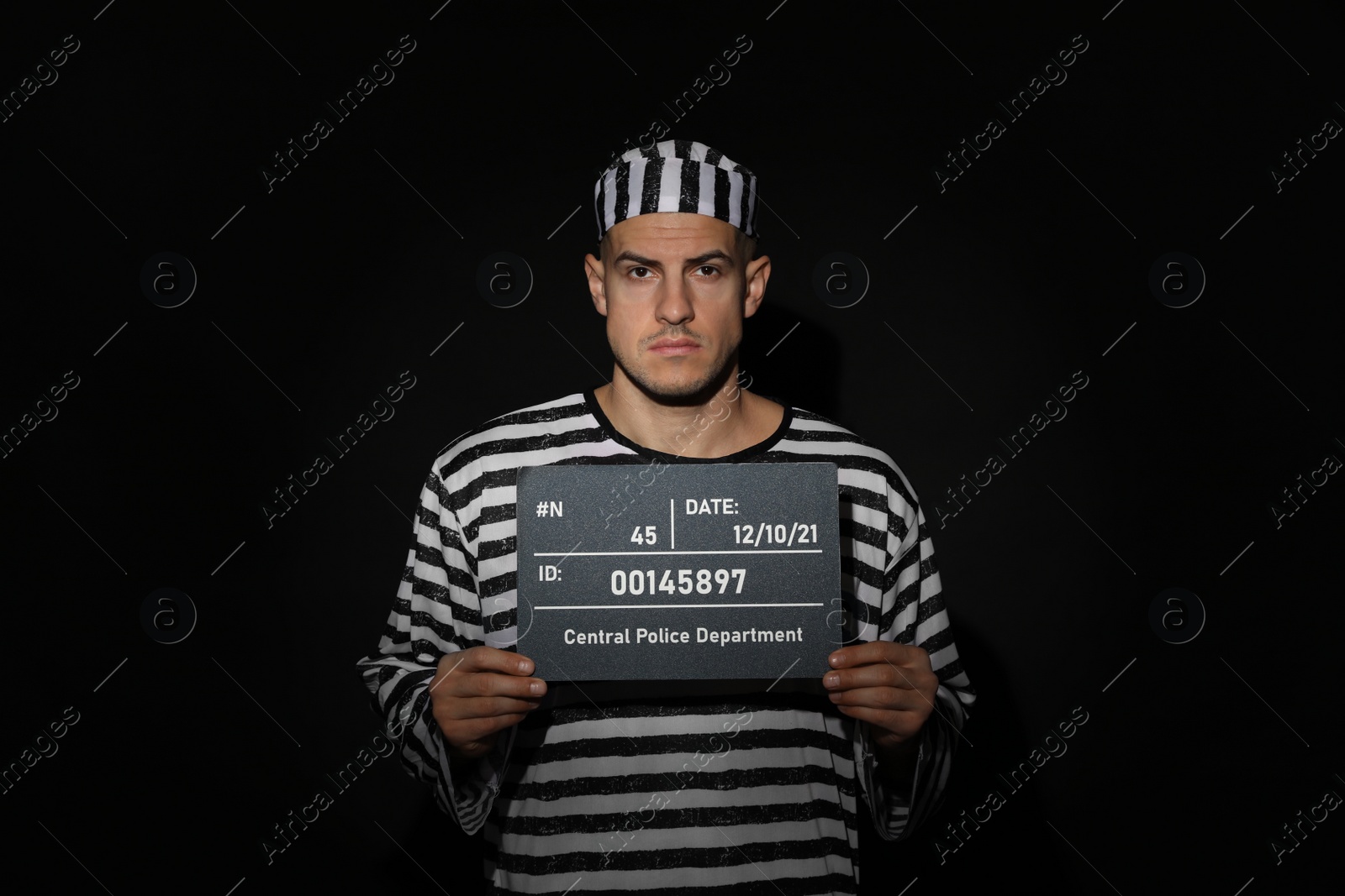 Photo of Mug shot of prisoner in striped uniform with board on black background, front view