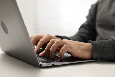 Photo of E-learning. Young man using laptop at white table, closeup