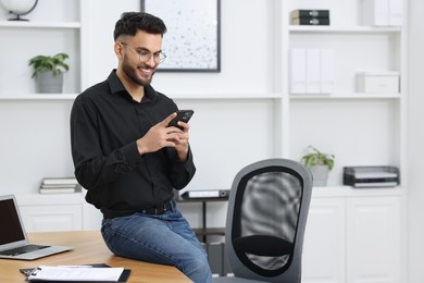 Happy young man using smartphone in office, space for text